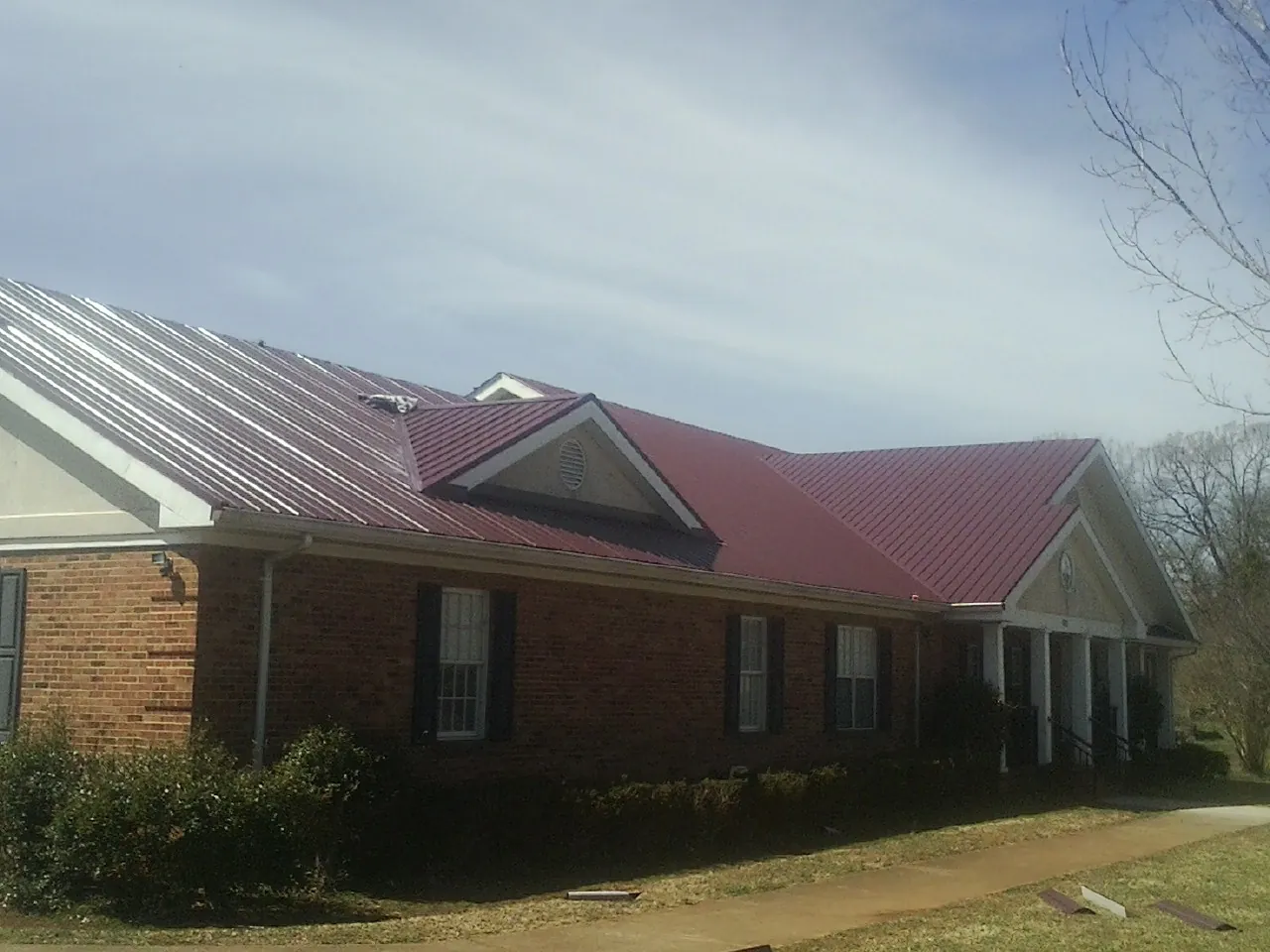 Red metal roof with gabled entries on a long brick building, from a Hail Damage Roof Repair job in Laguna Hills