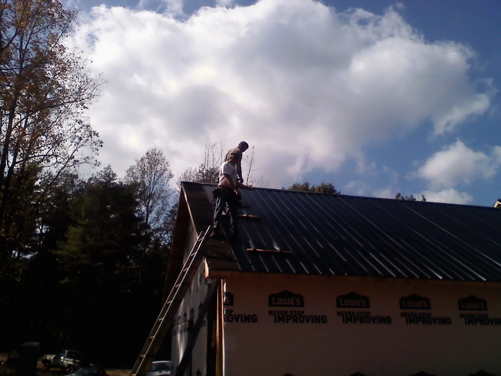 Roofer fastening dark metal panels high against a cloudy sky, from a Roof Inspection job in Laguna Hills