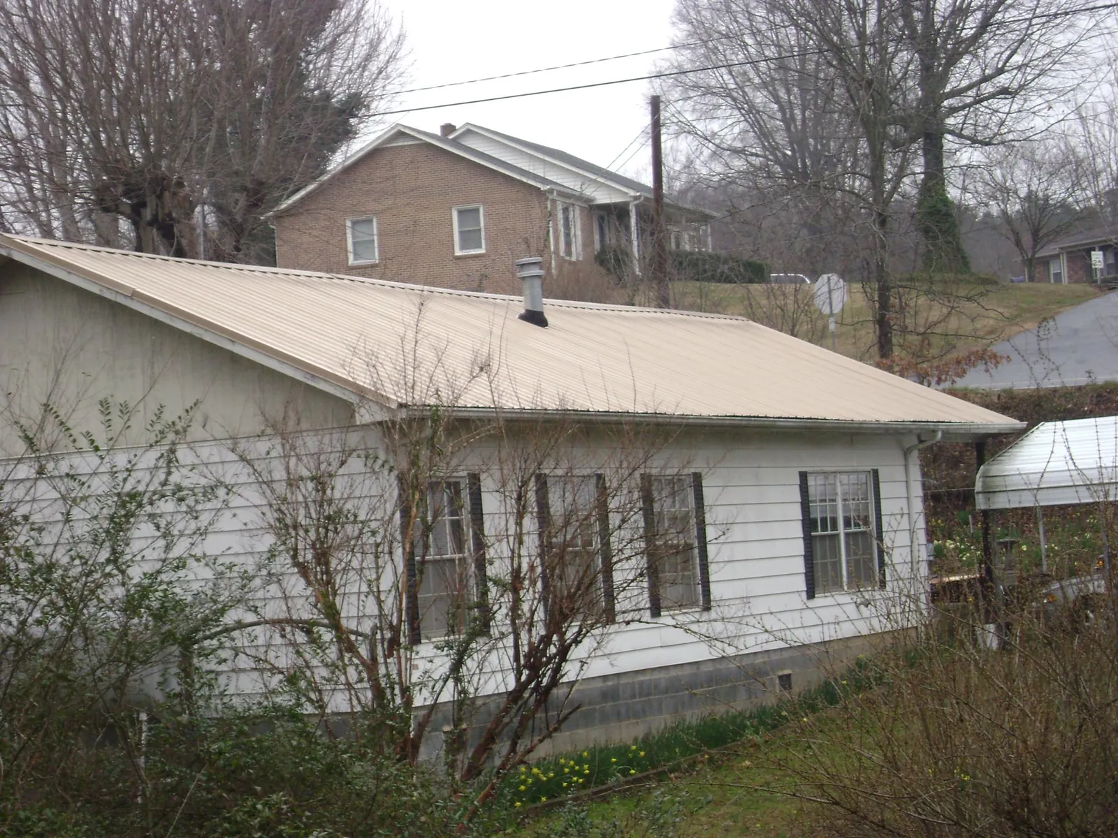 Tan metal roof on a white sided house set into a hillside — Commercial Roofing by Roofing Brothers in Laguna Hills